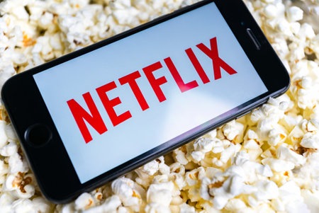 Uzhhorod, Ukraine. October 19, 2021 A man watches movies on Netflix. Internet service. on smartphone white image netflix phone lies on popcorn.のeditorial素材