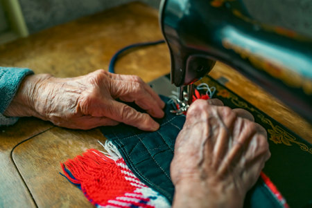 Senior woman in spectacles use sewing machine. wrinkled hands of the old seamstress.elderly woman ....