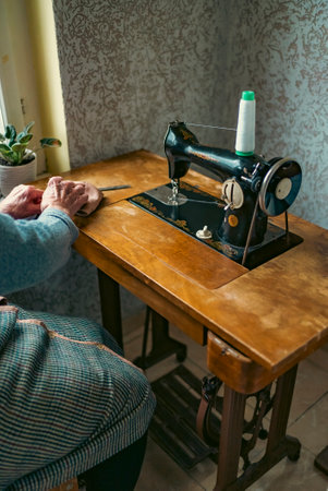 Senior woman in spectacles use sewing machine. wrinkled hands of the old seamstress.elderly woman ....