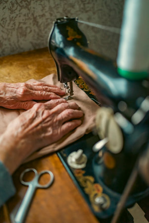 Senior woman in spectacles use sewing machine. wrinkled hands of the old seamstress.elderly woman . Old sewing machine Classic retro style manual sewing machine ready for sewing work.の写真素材