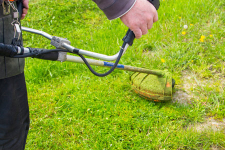 a man mows the grass with a chainsaw in the yard. the gardener is moving grass with a string lawn...