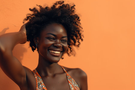 Joyful young woman with curly hair smiling against an orange background.の素材