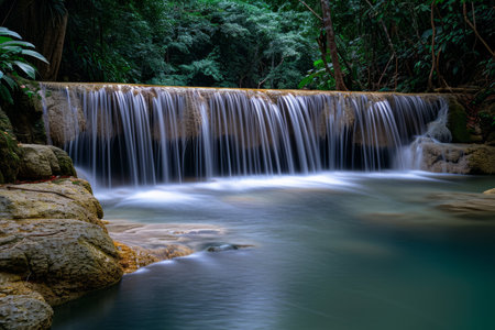 Tranquil waterfall in a lush forest with silky smooth water flowing over rocks, surrounded by greenery.の素材