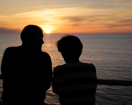 Silhouettes of Two People Gazing at the Ocean Sunsetの写真素材