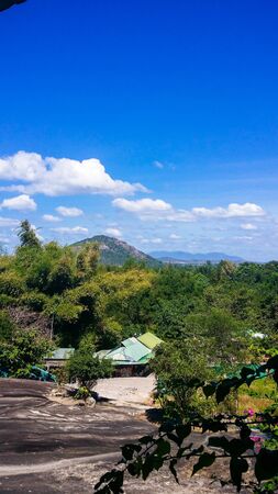 Blue sky, white clouds, green mountains, black stones and small houses on the mountainの写真素材