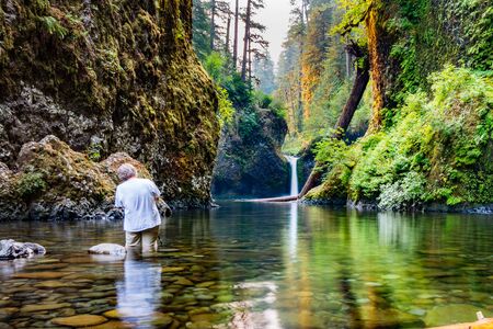 Landscape photographer stands in the river to take a photo of a waterfall in the Columbia River Gorgeの写真素材