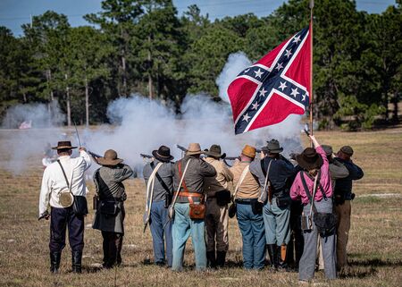 Brooksville, FL - January 18, 2020: Confederate battle flag flies over a group of civil war reenactors as they fire on the enemy.のeditorial素材