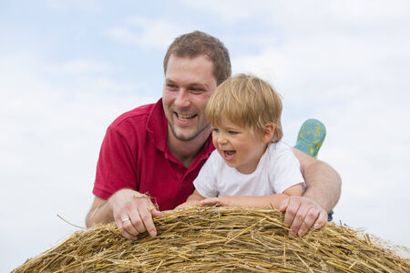 father and son lying on a bale of strawの写真素材