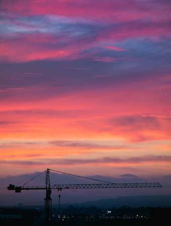 Single city crane against a pink, purple, orange, yellow, and blue sunset sky.の写真素材
