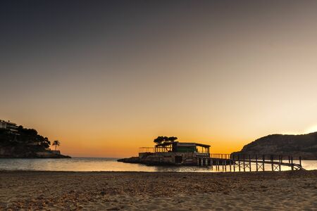 Chilling sea sunset in a calm beach of the bay with a small island and wooden bridgeの写真素材