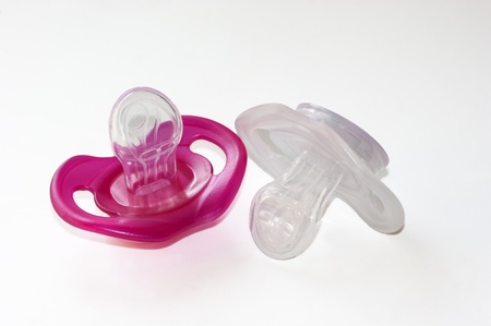 a pink and a white soother on white background