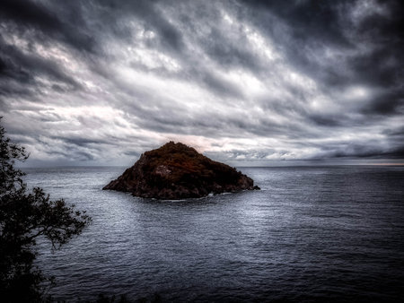 the island of bergeggi surrounded by the sea and a dramatic cloudy sky in the winter seasonの写真素材