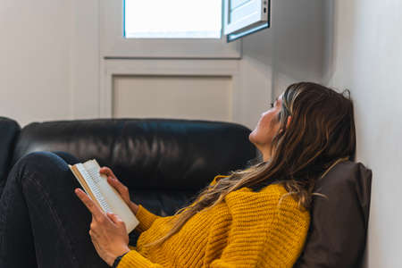 Young woman reading on the sofa in front of window