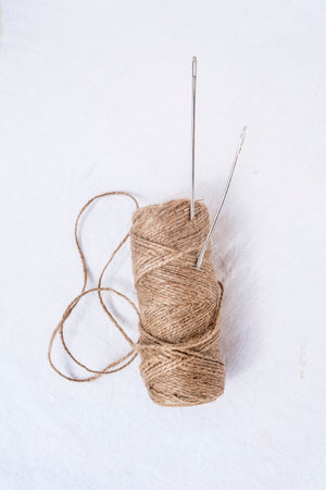 Spool of twine and sewing needles on a white background
