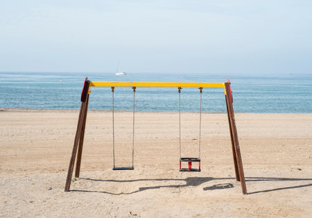 Wooden swing on the beach with sea in the background.