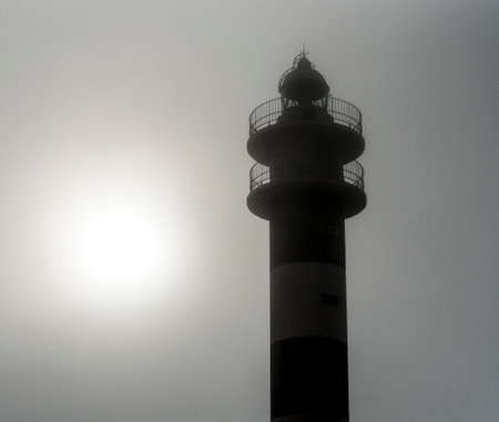 Lighthouse in the fog. The sun shines through the clouds.の写真素材