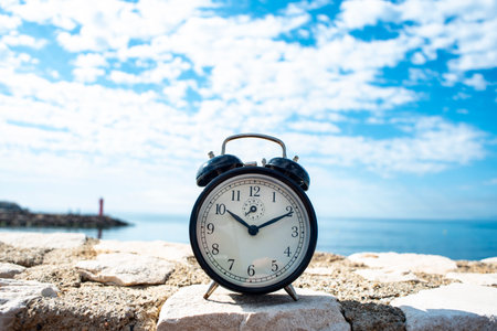 Alarm clock on the beach with blue sky and sea background.