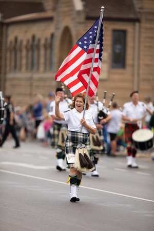 Peru, Indiana, USA - July 21, 2018 Woman carries the American flag leading the Indianapolis 500 Gordon Pipers Horse Shoe Pipes and Drums group of bagpipe players at the Circus City Festival Paradeのeditorial素材