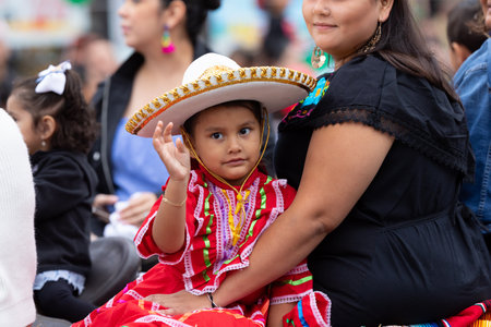 Chicago, Illinois, USA - September 8, 2019: 26th Street Mexican Independence Parade, girl on her mothers arms, wearing traditional clothing with a sombrero, waving at the spectatorsのeditorial素材