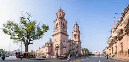 Morelia, Michoacan, Mexico - November 24, 2019: The Morelia Cathedral as seen from Mexico 15, and the Government Palace, people running and riding bikes on the roadのeditorial素材
