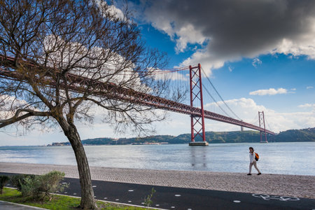LISBON, PORTUGAL - January 28, 2011: A woman walks along the banks of Tagus River in Belem and famouse bridge of 25th April over river on January 28, 2011, Lisbon, Portugalのeditorial素材