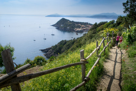 SESTRI LEVANTE, GENOA, ITALY - view of the promontory of Portofino and of the peninsula of Sestri Levante, from the path leading to Punta Manara, a typical view of the cliff that descends to the sea, with little girls walking the path, Liguria, Italyの写真素材