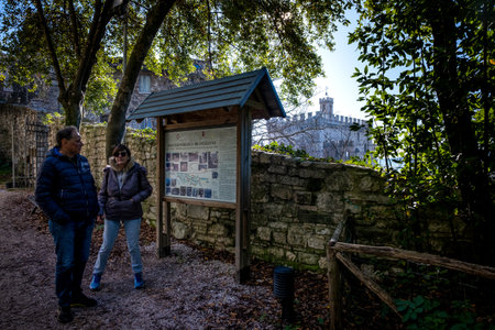 GUBBIO, ITALY - JANUARY 01, 2020: two unknown tourists check the signs in the Ranghiasci park in winter, in the background the ducal palace in Gubbio, a medieval town in Umbria in the province of Perugiaのeditorial素材