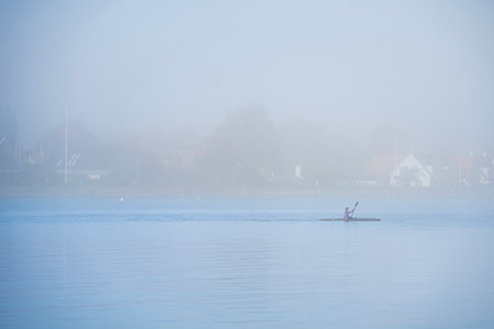 Keep fit rowing a canoe in the mist on a gloomy day. Healthy lifestyle kayaking in the fog. An...