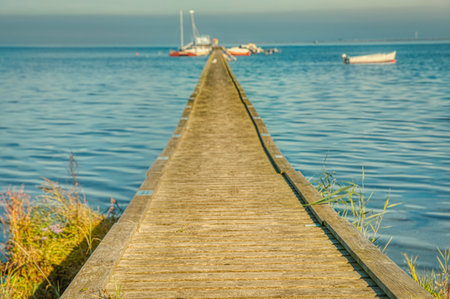 Wooden pier or jetty over the Baltic sea with mooring boats provides an illustration for summer vacation, seaside relaxation. Boardwalk or wharf over the sea conveys target aiming and purpose conceptの写真素材