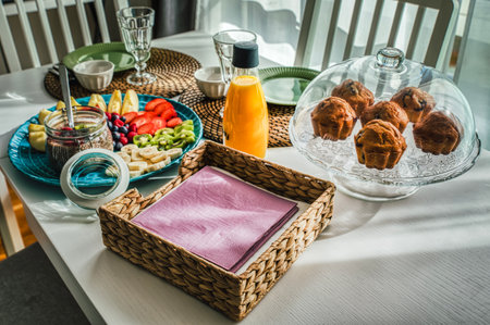 Morning continental breakfast with muffins and fruits like apples, strawberries, kiwis and banana on white table with rustic straw mat. Chia pudding and berries complete the Mediterranean organic mealの写真素材