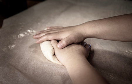 Closeup of child 's hands working fresh dough on a pastry board for making pizza, bread or pasta....