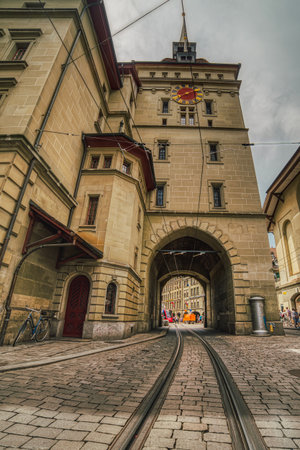 Bern, Switzerland June 06, 

Tram railway tunnel under the baroque tower Kafigturm on a historical cobbled street. Cablecar track or tracks across the arched medieval steeple in the popular Marktgasseのeditorial素材