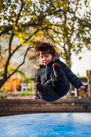 Child with puffy face and clumsy hair flying with joy on a soft inflatable trampoline. Boy jumping on a air bouncer is sitting in the air while landing on a morbid surface. Trust and security conceptの写真素材
