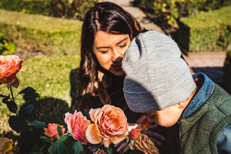 A small kid smelling the delicate fragrance of a rose with his mom. Child with his mother sniffing a...