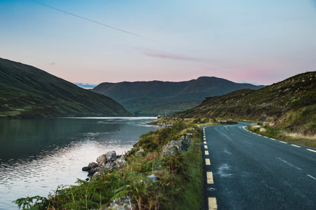 Connemara loop or road as the sun sets on Killary Fjord, Connemara National Park. Western Ireland sunset as the scenic N59 route stretches beside the calm ocean water surrounded by mountains. Irelandの写真素材