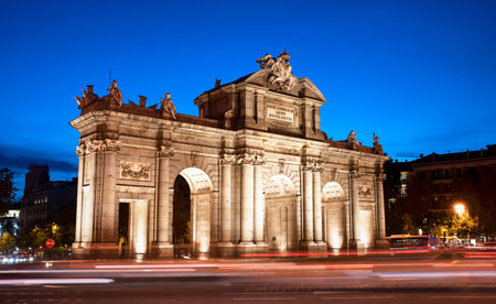 Puerta de AlcalÃ¡ by the entrance of El Retiro park at blue hour in Madrid. Puerta Alcala evening view with car light trails as the night approaches. Spanish downtown vibeの写真素材