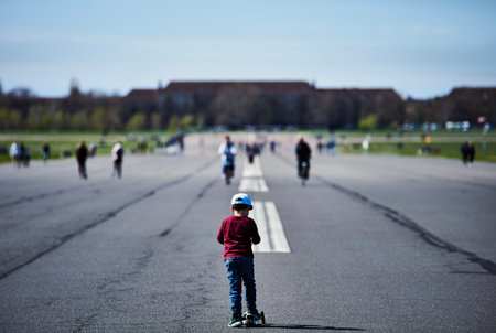 Child running with a scooter on an airport runway. Young boy on a large airfield tarmac with people...