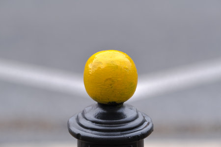 single yellow metal ball on street post, blurred street in the background, white lines symmetryの写真素材