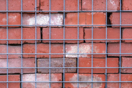 red brick wall behind wire metal fence, abstract background and symmetryの写真素材