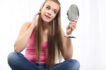 Young long-haired blonde girl sitting on the bed and looks at the mirrorの写真素材