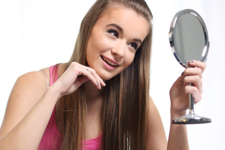 Young long-haired blonde girl sitting on the bed and looks at the mirrorの写真素材