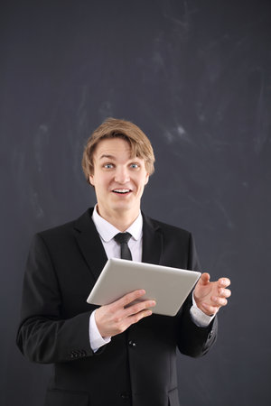 Young, handsome man on black hold a tablet on chalkboard background の写真素材
