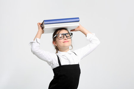 Girl in school uniform on a white background with books on her headの写真素材