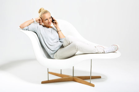 Blonde talking on mobile phone while sitting on a stylish white chairの写真素材