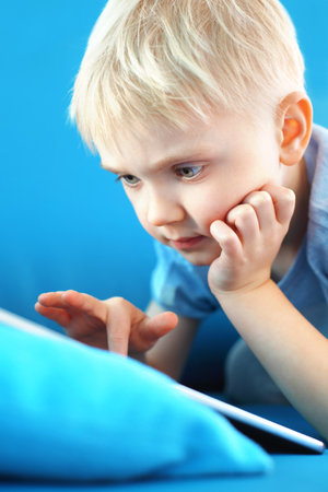 Little boy, preschooler with a digital tablet on a blue backgroundの写真素材