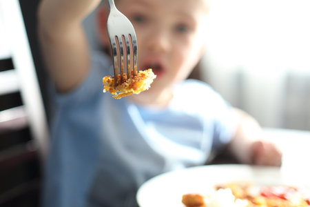 Child while eating. The little boy during a meal shows chop stamped on a fork.の写真素材