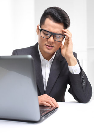 Handsome man in business suit sitting at his desk in his study supports the head in his hands.の写真素材