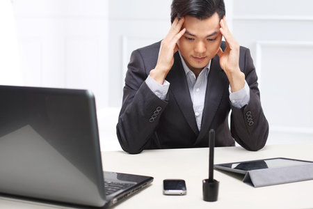 Handsome man in business suit sitting at his desk in his study supports the head in his hands.の写真素材
