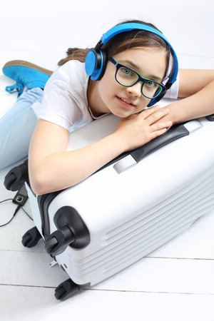 Girl in blue headphones packed a suitcase with things for a holiday tripの写真素材