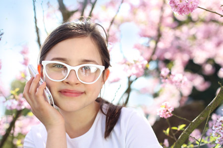 A girl talking on a cell phone while standing under a tree floweredの写真素材